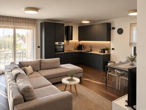Ein modernes Wohnzimmer mit einer Eckcouch, einem kleinen runden Tisch mit einer Pflanze und einem Essbereich mit Tisch und Stühlen.