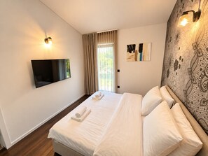 A hotel room with a bed, a flat-screen TV mounted on the wall, a window with curtains, and a patterned wall. - Villa Casa Vesta - Two Bedroom Villa, Sleeps 4 (Sveti Ivan)