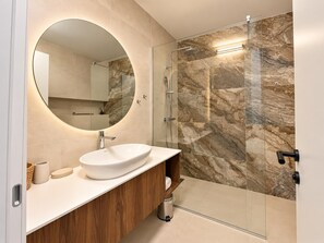 Ein modernes Badezimmer mit rundem Spiegel, weißem Waschbecken und einer Duschkabine aus Glas.
