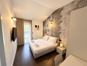 Ein Hotelzimmer mit Bett, Nachttisch, an der Wand montiertem Fernseher und einem Fenster mit Vorhängen.