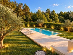 Ein rechteckiger Swimmingpool mit einer gefliesten Liegefläche, umgeben von gepflegtem Rasen und Bäumen.