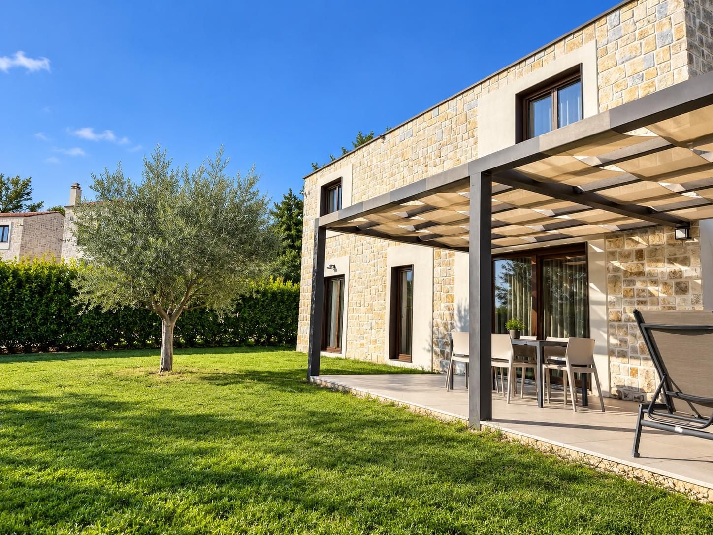 A modern house with a stone facade, a covered patio with outdoor furniture, and a well-maintained lawn.