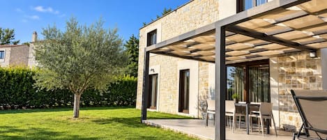 A modern house with a stone facade, a covered patio with outdoor furniture, and a well-maintained lawn.