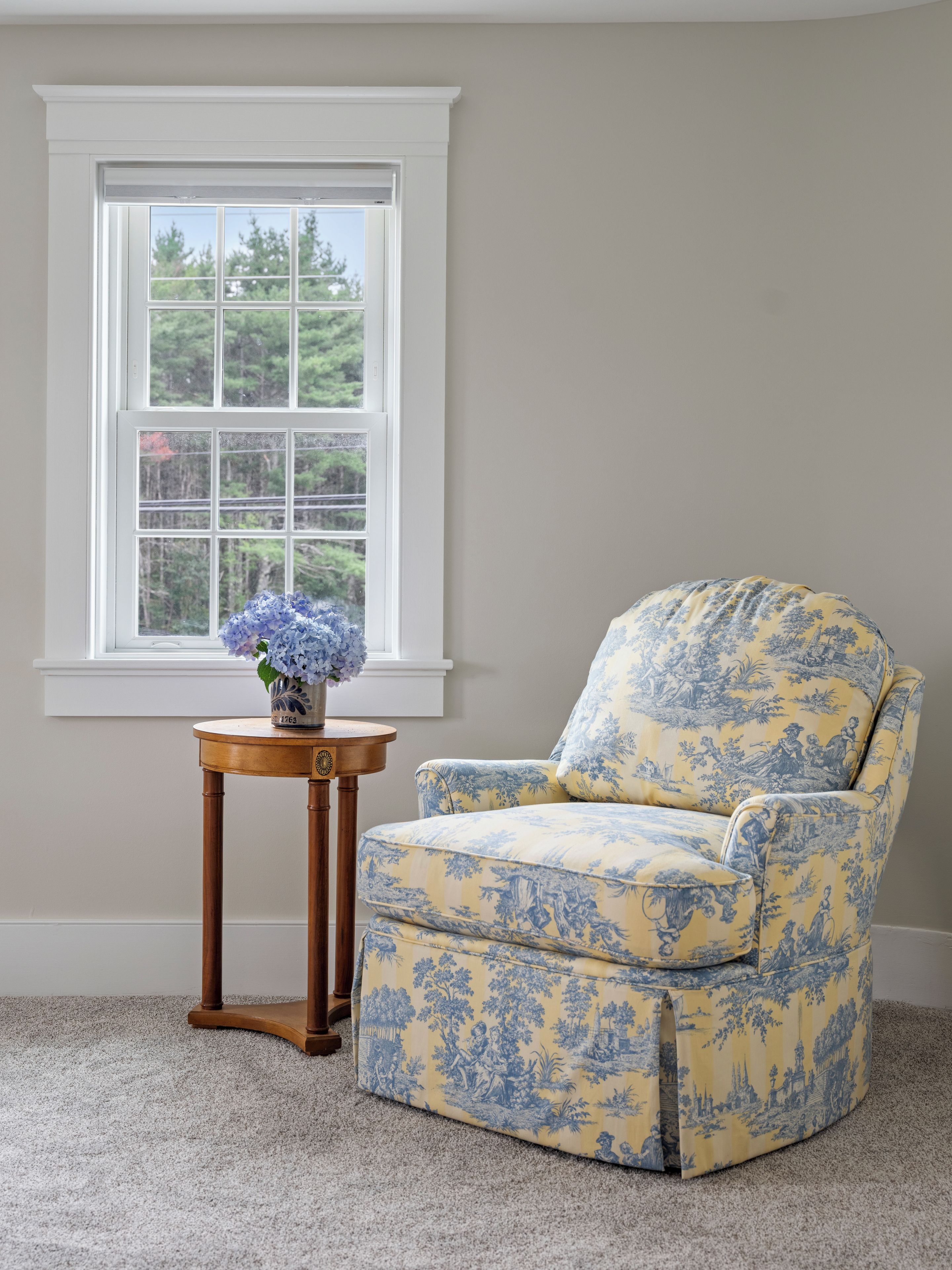 A room with a window, a chair, and a small table with a vase.