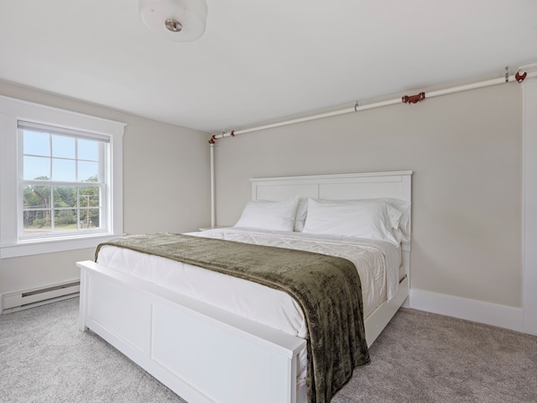A bedroom with a white bed, a window, and a white ceiling.