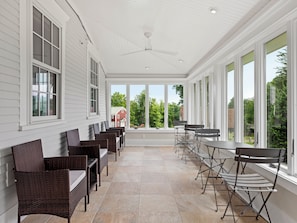 A covered patio with wicker furniture and large windows offering views of a red building and greenery. - Chestnut Inn (Sandwich)
