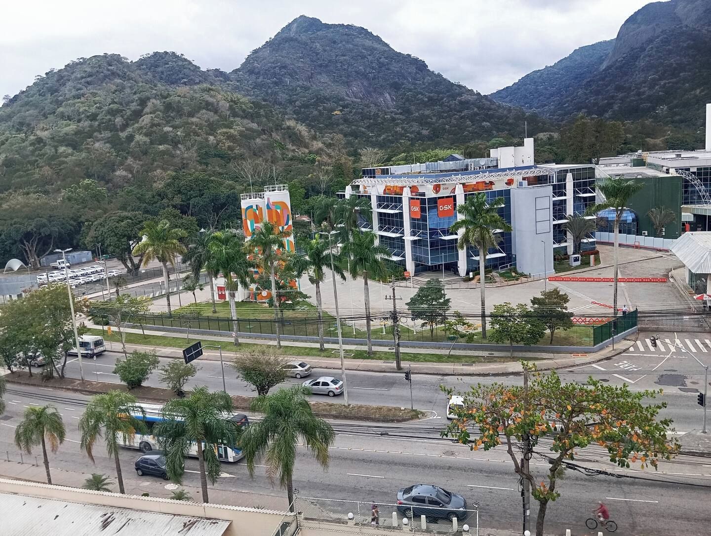A modern building with a prominent GSK sign, surrounded by palm trees and a mountainous backdrop.