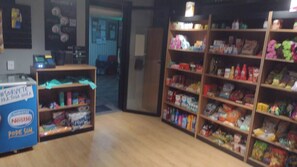 A store interior with shelves stocked with various products, a blue display with a Nestle logo, and a counter with a cash register.
