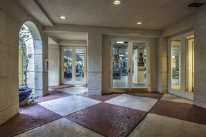 Corredor com piso de azulejos, portas de vidro que dão para uma academia e uma parede de pedra.