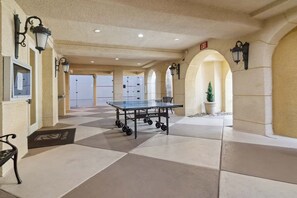 Amplo espaço interno com mesa de pingue-pongue, balcão de recepção e planta em vaso.