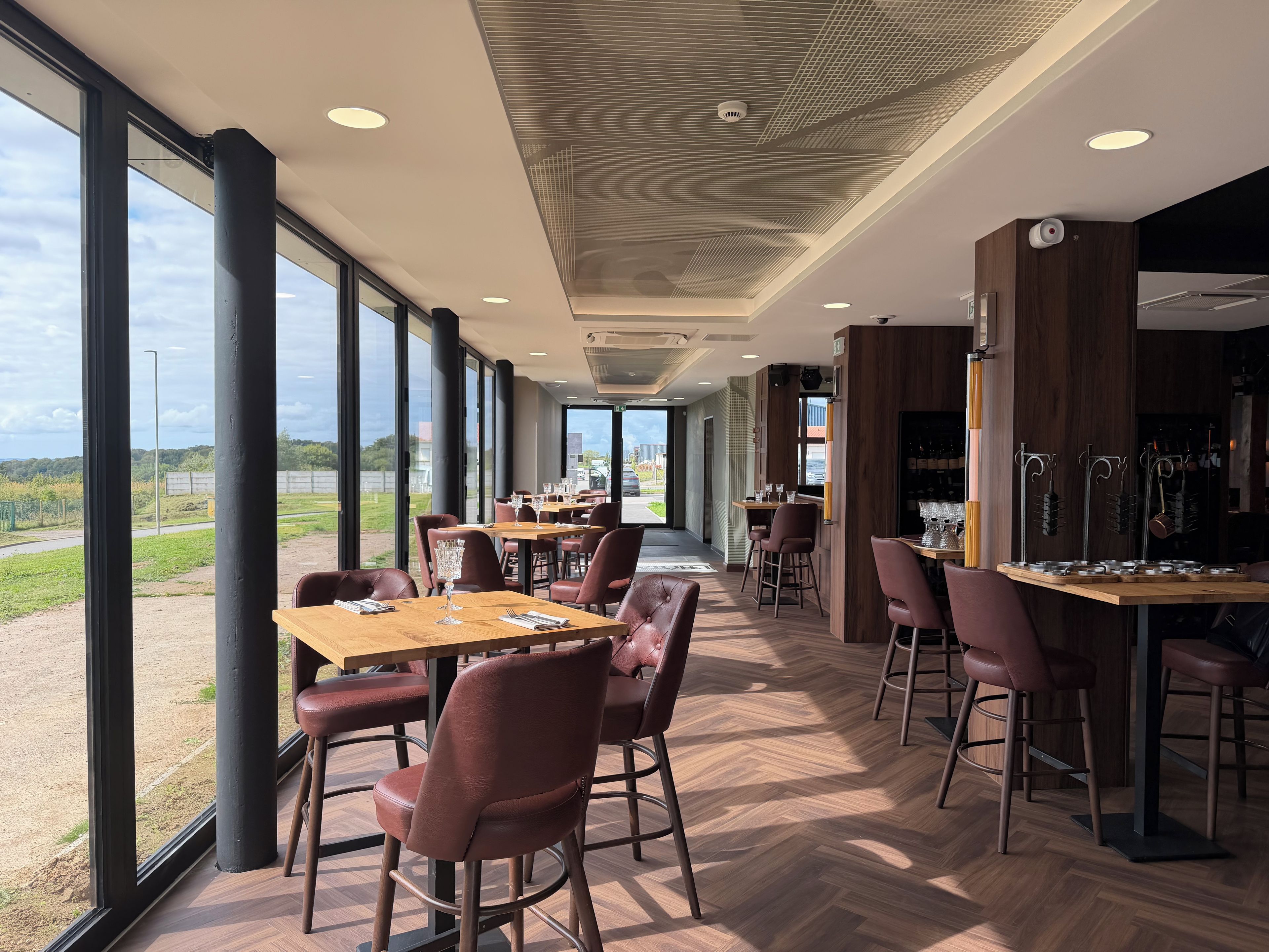 Een restaurant met grote ramen, houten vloeren en een bar.