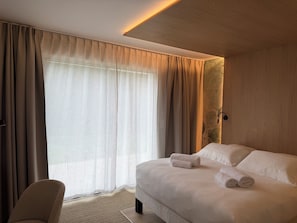 Habitación de hotel con una cama grande, una silla y un ventanal con cortinas.