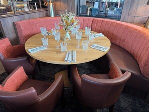 Una mesa redonda con superficie de madera, rodeada de sillas con asientos acolchados de tela roja.