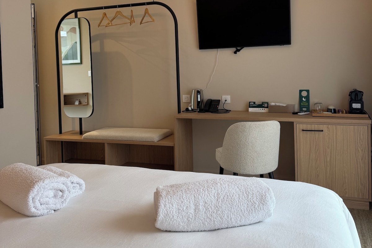 Habitación de hotel con cama, escritorio, silla, televisor de pantalla plana y espejo.