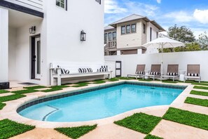 A swimming pool with a white exterior, surrounded by grass and a white deck with lounge chairs. - Stepping Stone Main House (Panama City Beach)