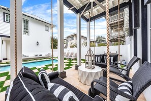 A covered outdoor seating area with swings, a pool, and a lawn. - Stepping Stone Main House (Panama City Beach)