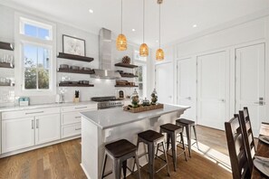 Een moderne keuken met witte kasten, een centraal eiland met krukken, hanglampen en een groot raam.