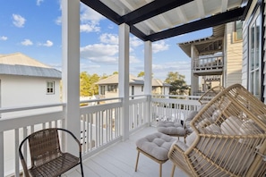A covered outdoor balcony with wicker furniture and a white railing. - Stepping Stone Main House (Panama City Beach)