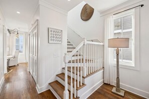 A staircase with white railings and wooden steps, a wall-mounted lamp, and a framed picture on the wall. - Stepping Stone Main House (Panama City Beach)