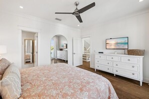 A bedroom with a bed, dresser, TV, and a ceiling fan. - Stepping Stone Main House (Panama City Beach)