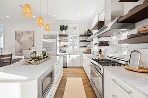 A modern kitchen with white cabinetry, a central island, and pendant lighting. - Stepping Stone Main House (Panama City Beach)