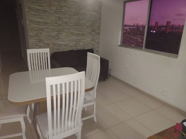 A dining area with a white table and chairs, a black sofa, and a window with a cityscape view.