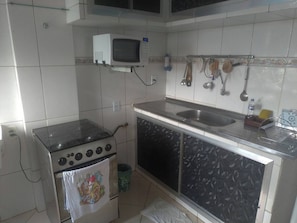 A kitchen with a stove, microwave, sink, and hanging utensils.
