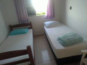 A small, single-room accommodation with two single beds, a wooden chair, and a window with curtains.