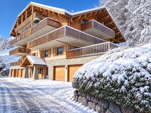 A multi-story wooden chalet with balconies, stone walls, and a snow-covered landscape. - Le Jardin Alpin A 41 - Les Balcons de Suzanne (Vaujany)