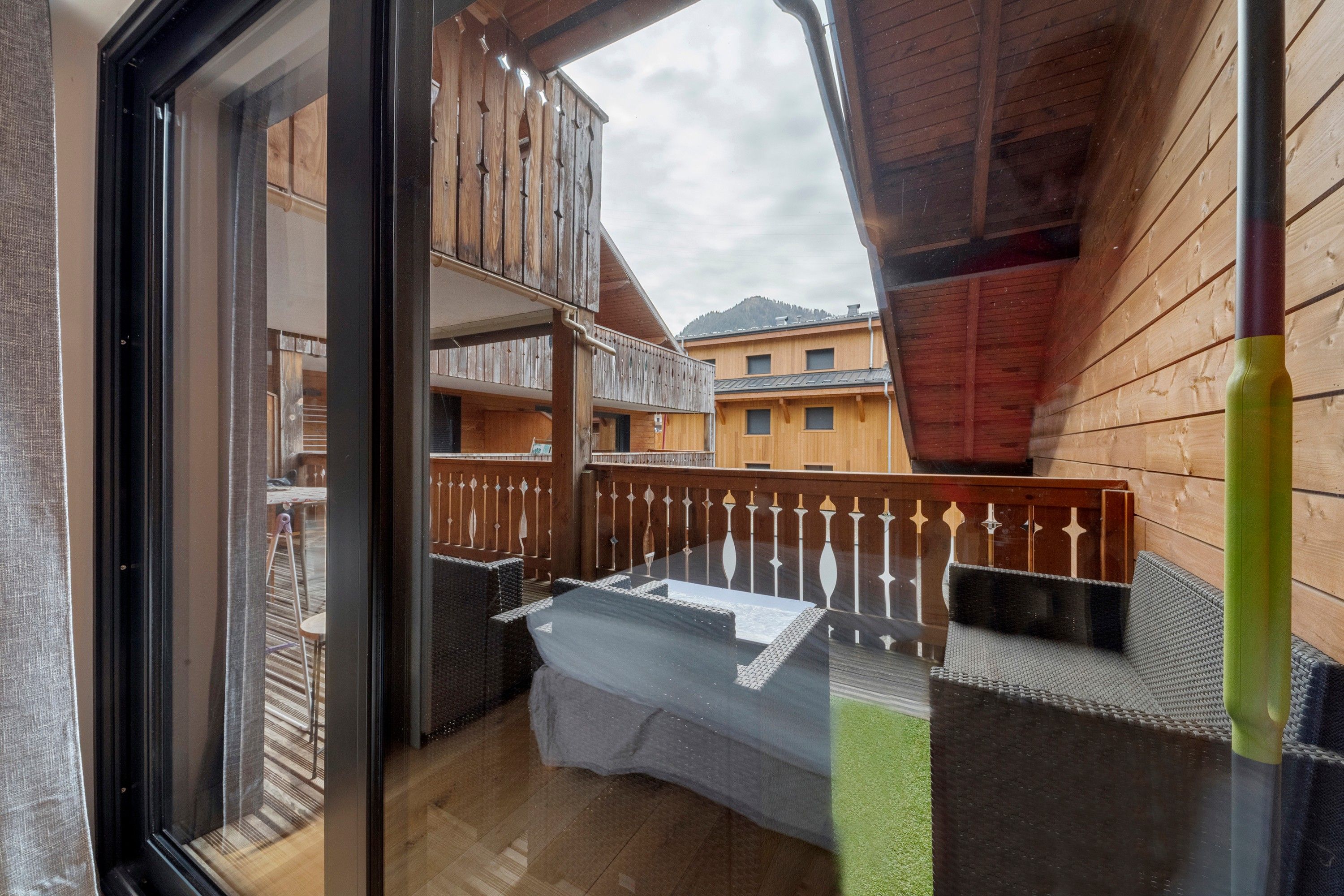 Un balcon en bois, agrémenté d’une table et de chaises, donnant sur un quartier résidentiel avec des maisons.