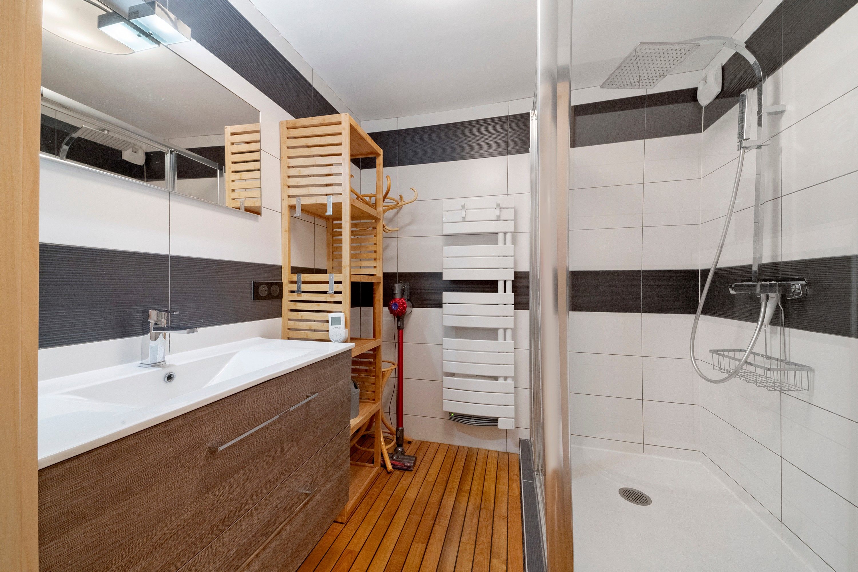 Een moderne badkamer met een houten wastafelmeubel, een douche met glazen deur en een inbouwplank.