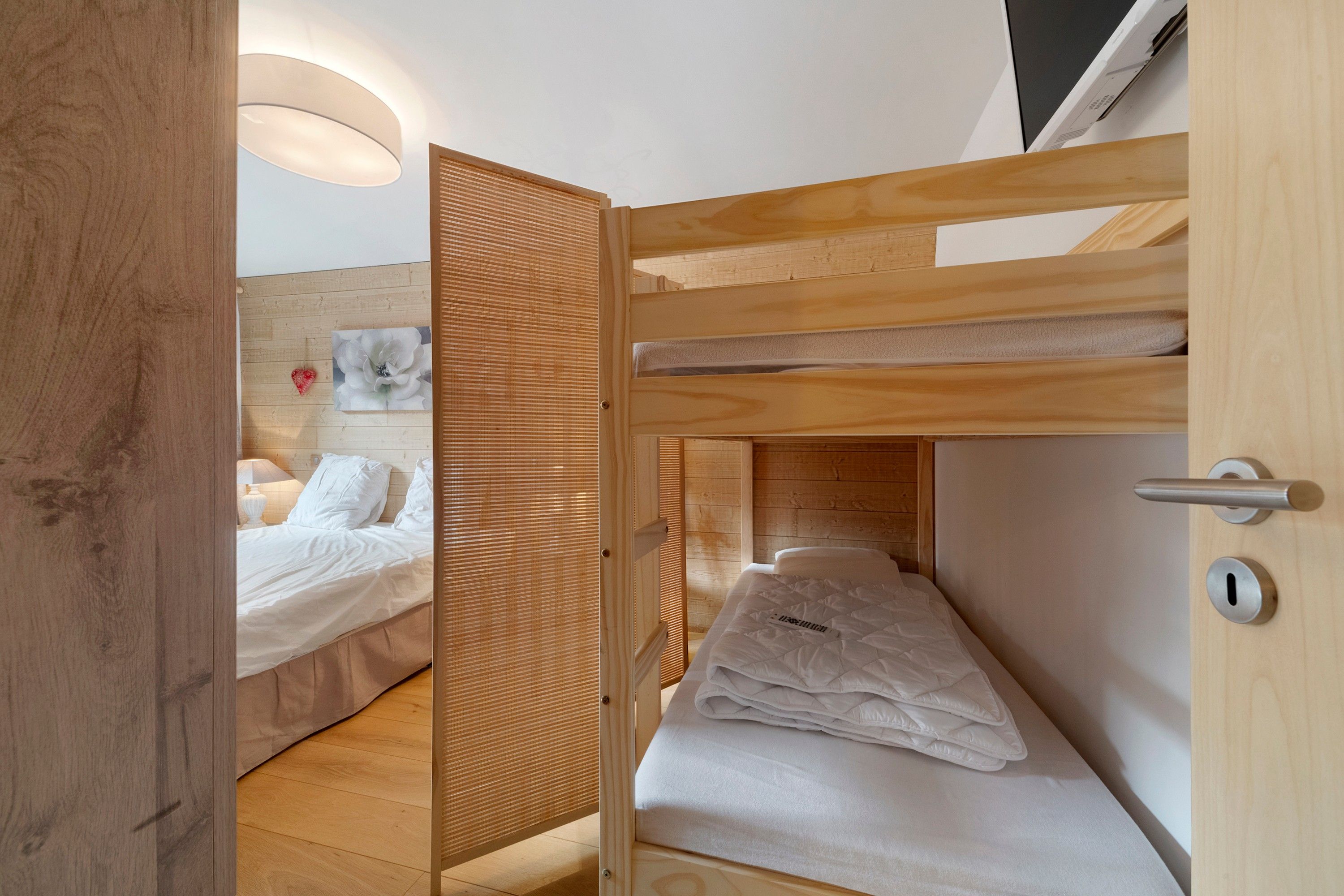 Une chambre avec un lit superposé, une table de chevet avec une lampe et une étagère murale avec un tableau.