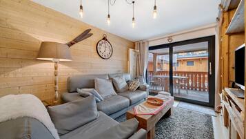 Een gezellige woonkamer met een bank, een lamp, een klok en uitzicht op het exterieur.