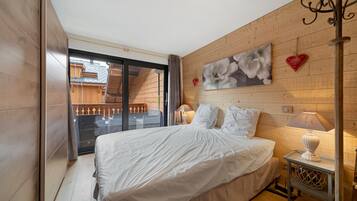 Een slaapkamer met een groot bed, een houten wand, een bloemstillevoering, een lamp en uitzicht op een balkon.