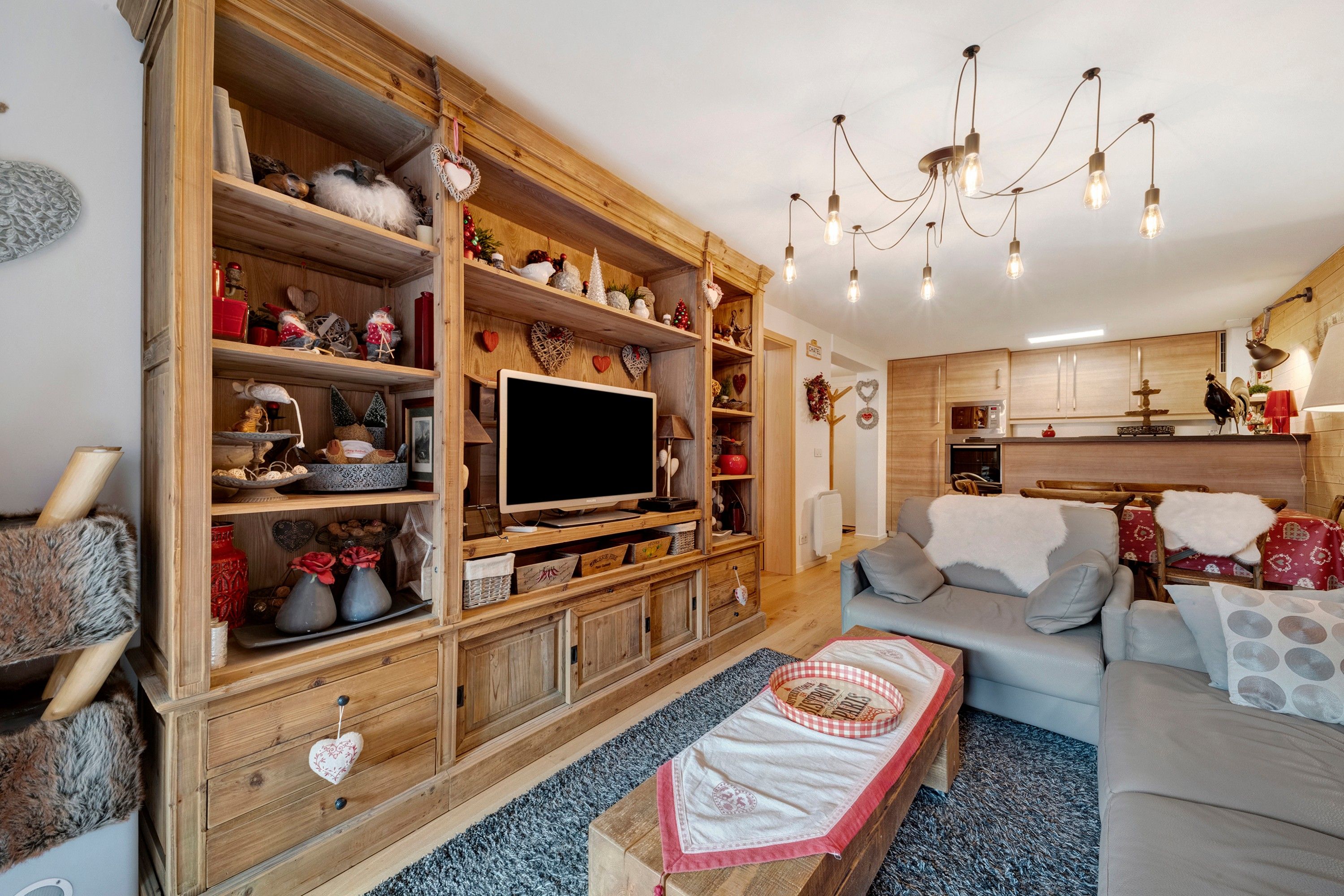 Ein gemütliches Wohnzimmer mit Holzbögen, einem Flachbildfernseher, einer Couch und einer Kristallleuchter.