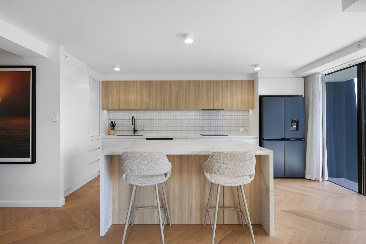 A modern kitchen with a wooden countertop, two bar stools, and a built-in refrigerator.