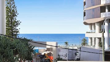 A view of a building with a balcony overlooking the sea, construction equipment, and a truck parked in front.