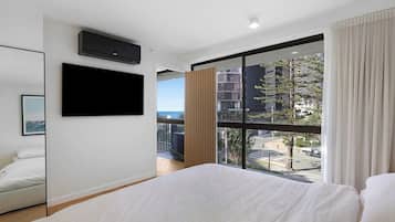 A hotel room with a large bed, a mounted TV, a window with a view of buildings and a street, and a balcony.