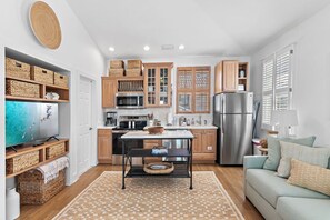 A compact kitchen with wooden cabinets, a stainless steel refrigerator, and a dining table. - Palms by the Sea Carriage House | Community Pool | Pets Welcome (Seacrest Beach)