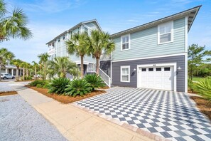 A two-story residential building with a garage, a checkered driveway, and palm trees. - Palms by the Sea Carriage House | Community Pool | Pets Welcome (Seacrest Beach)