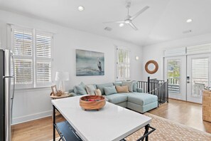 A modern kitchen with a white countertop, a dining table, and a blue sofa. - Palms by the Sea Carriage House | Community Pool | Pets Welcome (Seacrest Beach)