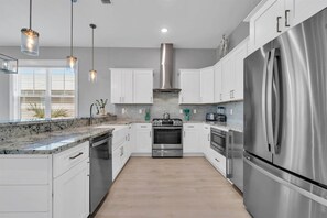 A modern kitchen with white cabinets, stainless steel appliances, and pendant lighting. - ⭐Palms By The Sea | Rooftop Deck | Pool | Beach Access⭐ (Seacrest Beach)