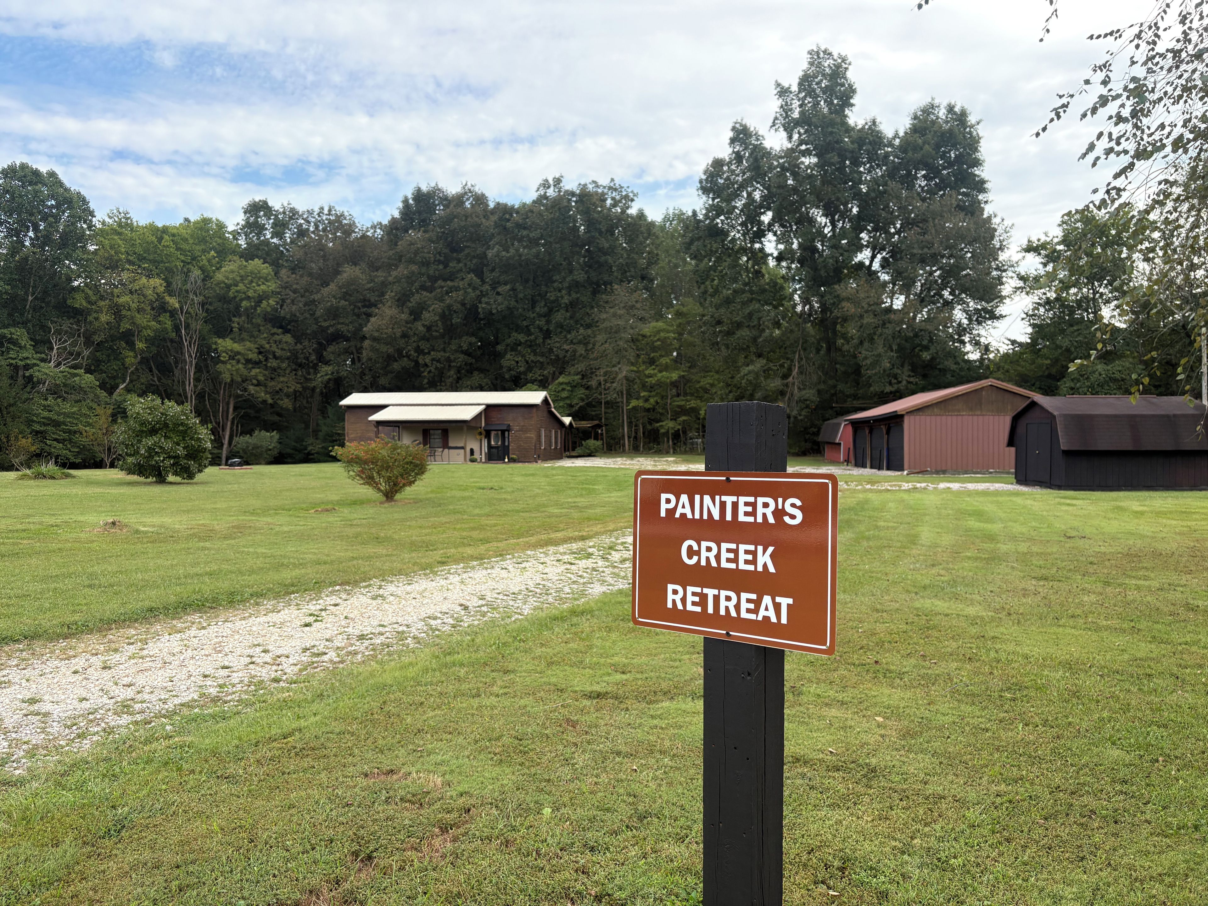 A sign for Painter's Creek Retreat with a grassy field and buildings in the background.