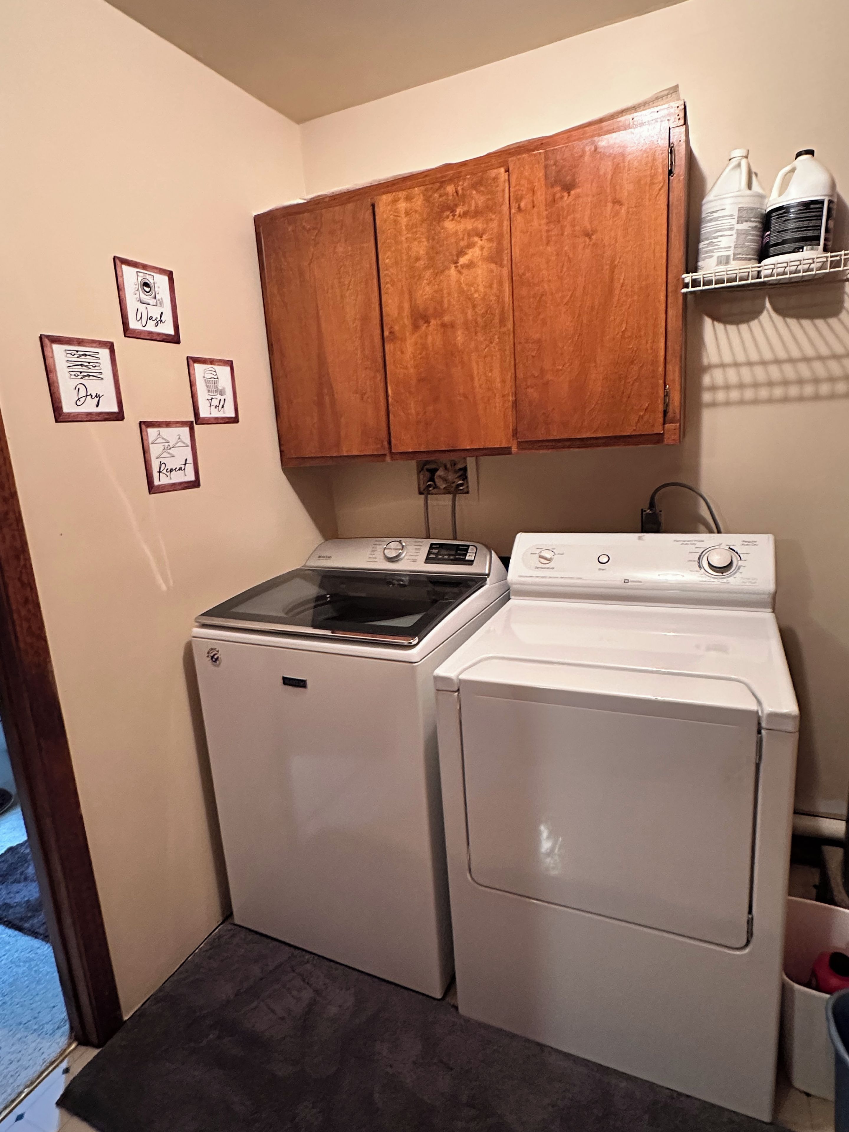 A laundry room with a washer and dryer, wooden cabinets, and framed instructions on the wall.