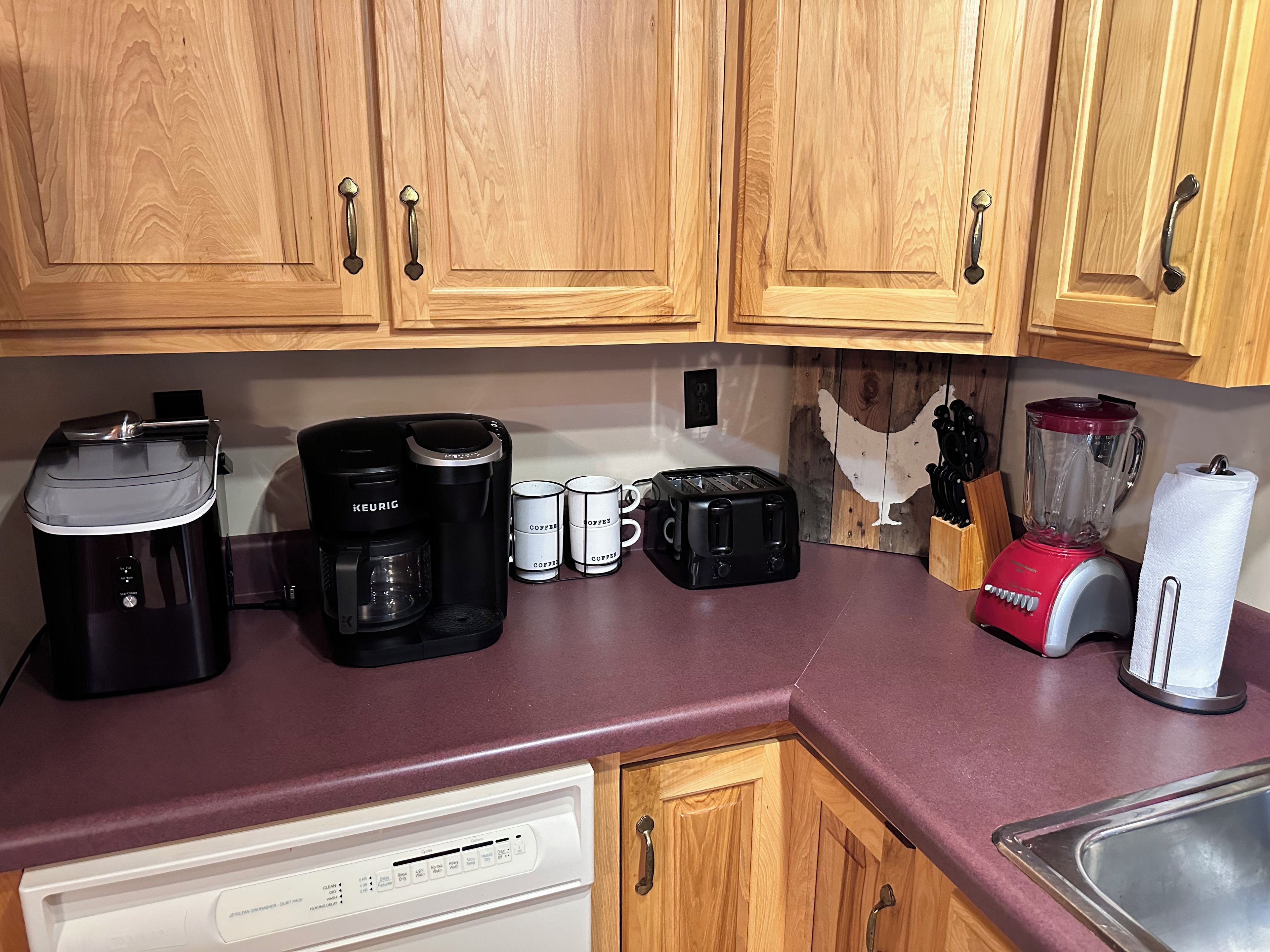 Una cocina con armarios de madera, cafetera, tostadora, licuadora y lavavajillas.