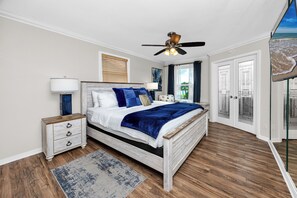 A bedroom with a bed, nightstand, lamp, ceiling fan, and a view of the beach through a door. - Amazing Waterfront Home 2 Blks 2 Beach & Food (Indian Rocks Beach)