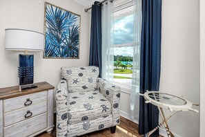 A room with a view of a beach, a chair with a nautical pattern, a lamp, and a small ironing board. - Amazing Waterfront Home 2 Blks 2 Beach & Food (Indian Rocks Beach)