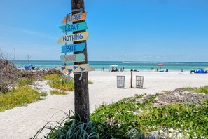 Une scène de plage avec un panneau indicateur, une plage de sable, des parasols et des personnes.