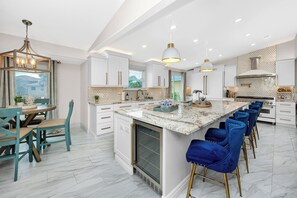A modern kitchen with white cabinetry, a marble island, and blue bar stools. - Amazing Waterfront Home 2 Blks 2 Beach & Food (Indian Rocks Beach)