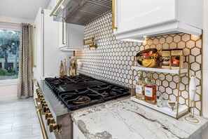 A modern kitchen with a gas stove, white marble countertop, and a honeycomb-patterned backsplash. - Luxury Waterfront Heated Pool Dock Golf Cart (Indian Rocks Beach)